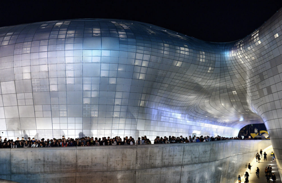 Night view of Dongdaemun Design Plaza (DDP) with visitors gathered outside, a highlight of modern architecture in a Seoul 2-day itinerary