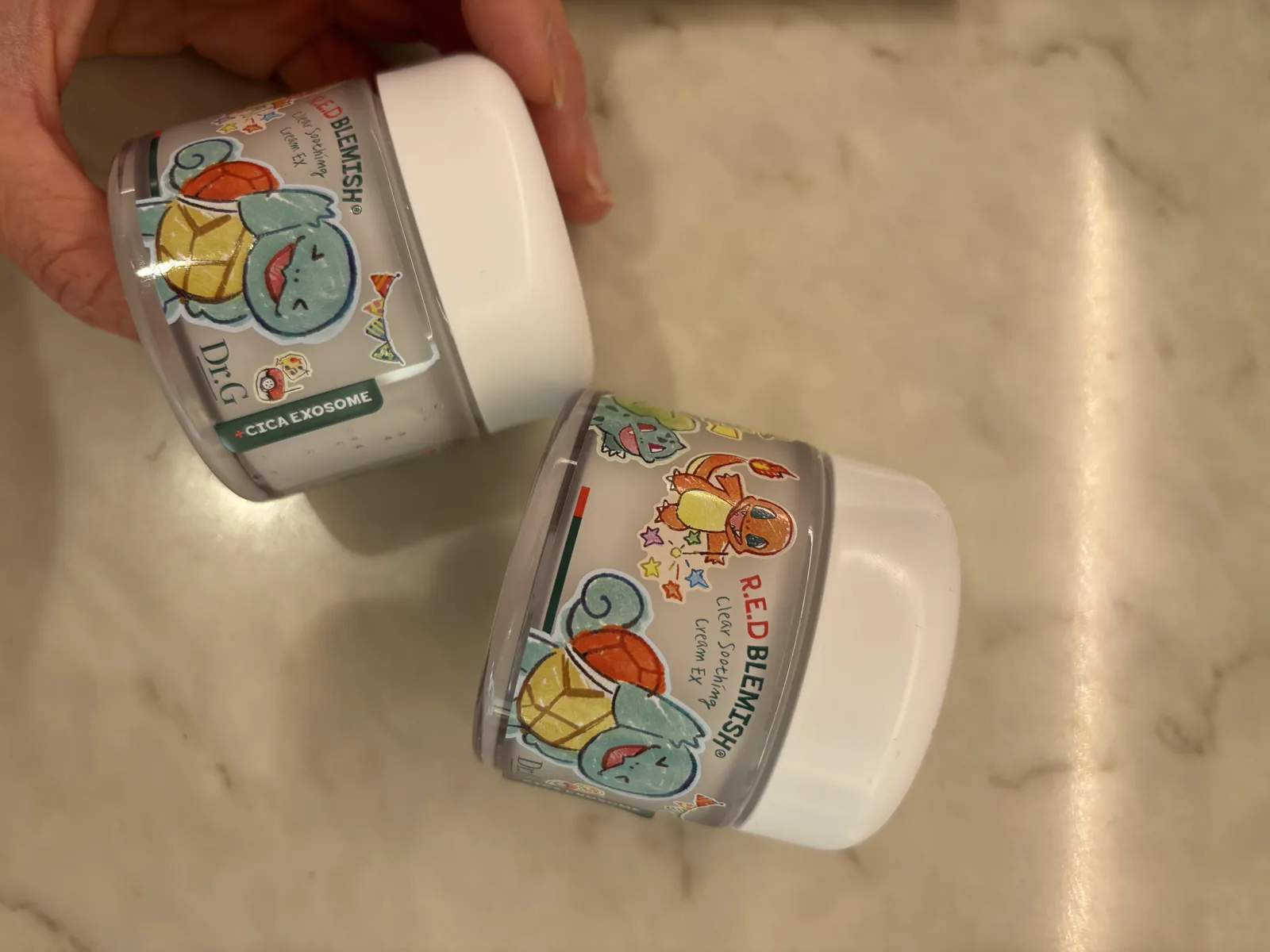 Dr.G Red Blemish Serum line context with the matching R.E.D Blemish soothing cream jars held in hand