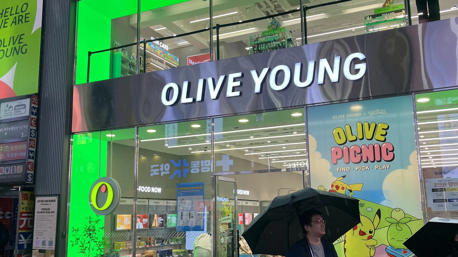 Olive Young Myeongdong flagship storefront glowing on a busy rainy street