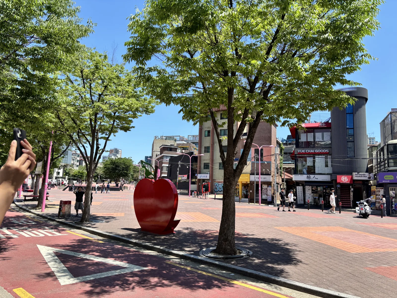Wide red-paved Hongdae shopping street with shoppers and storefronts on a sunny day