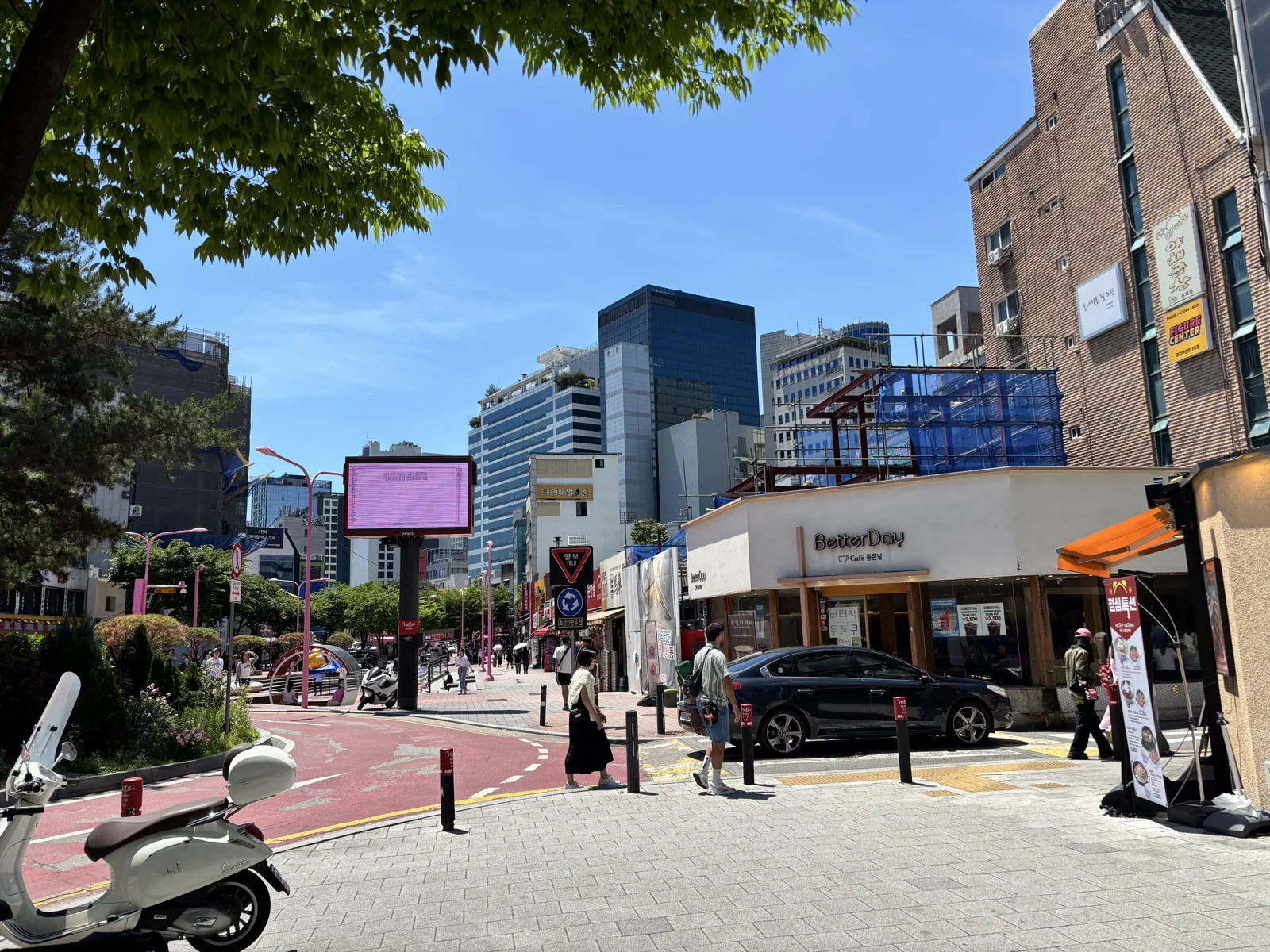 Corner of the Hongdae shopping street with a digital screen and street-level cafes