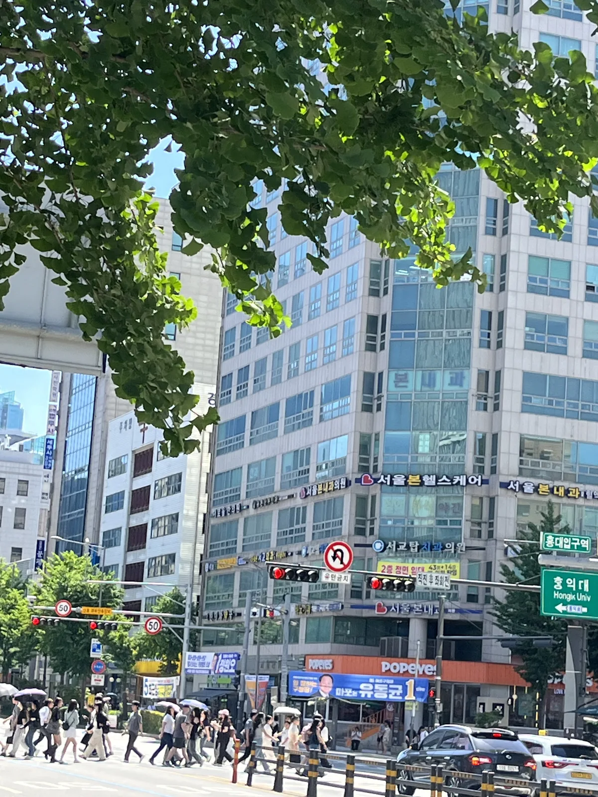 Crowds crossing at Hongik University Station on a summer afternoon in Hongdae