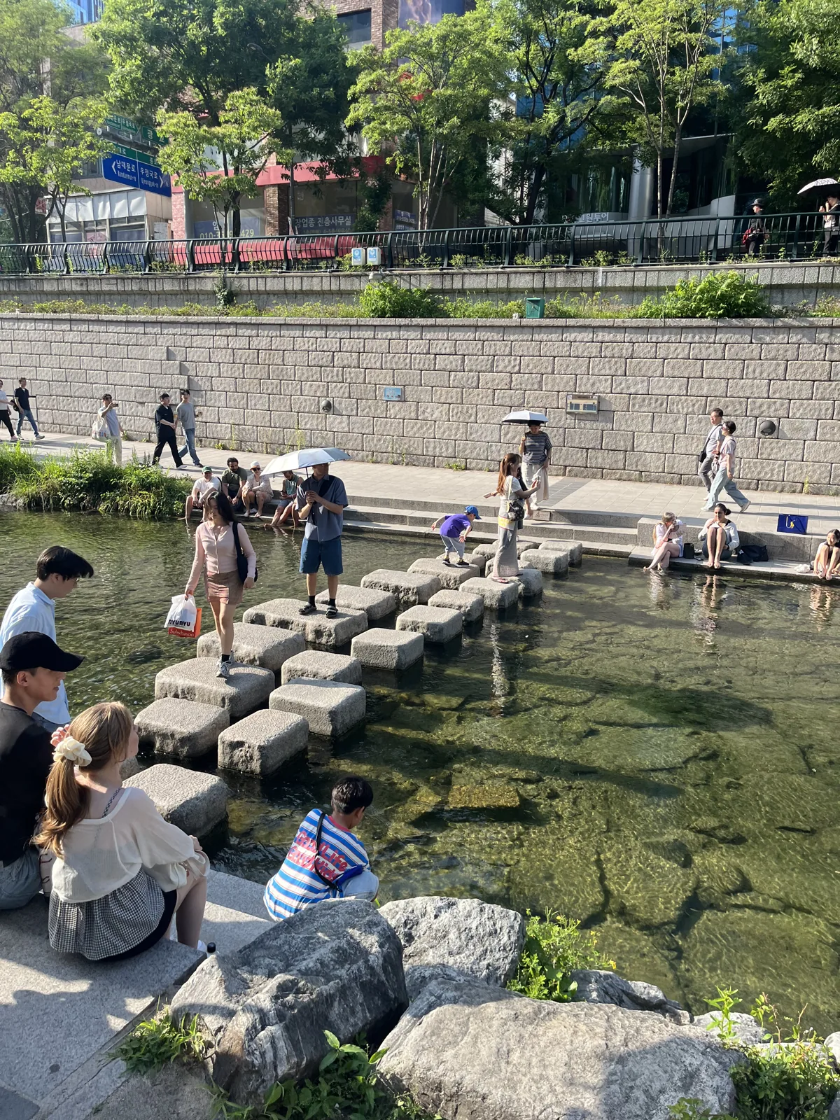 Cheonggyecheon stream walk in Seoul with people crossing the stepping stones below city towers