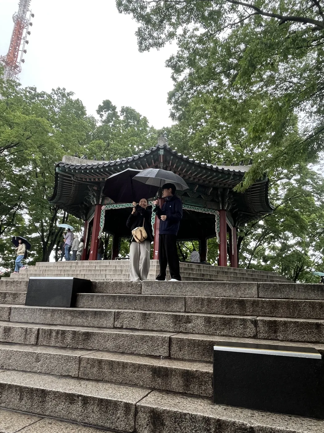 Namsan in the rain with visitors sheltering under the pavilion on the plaza steps