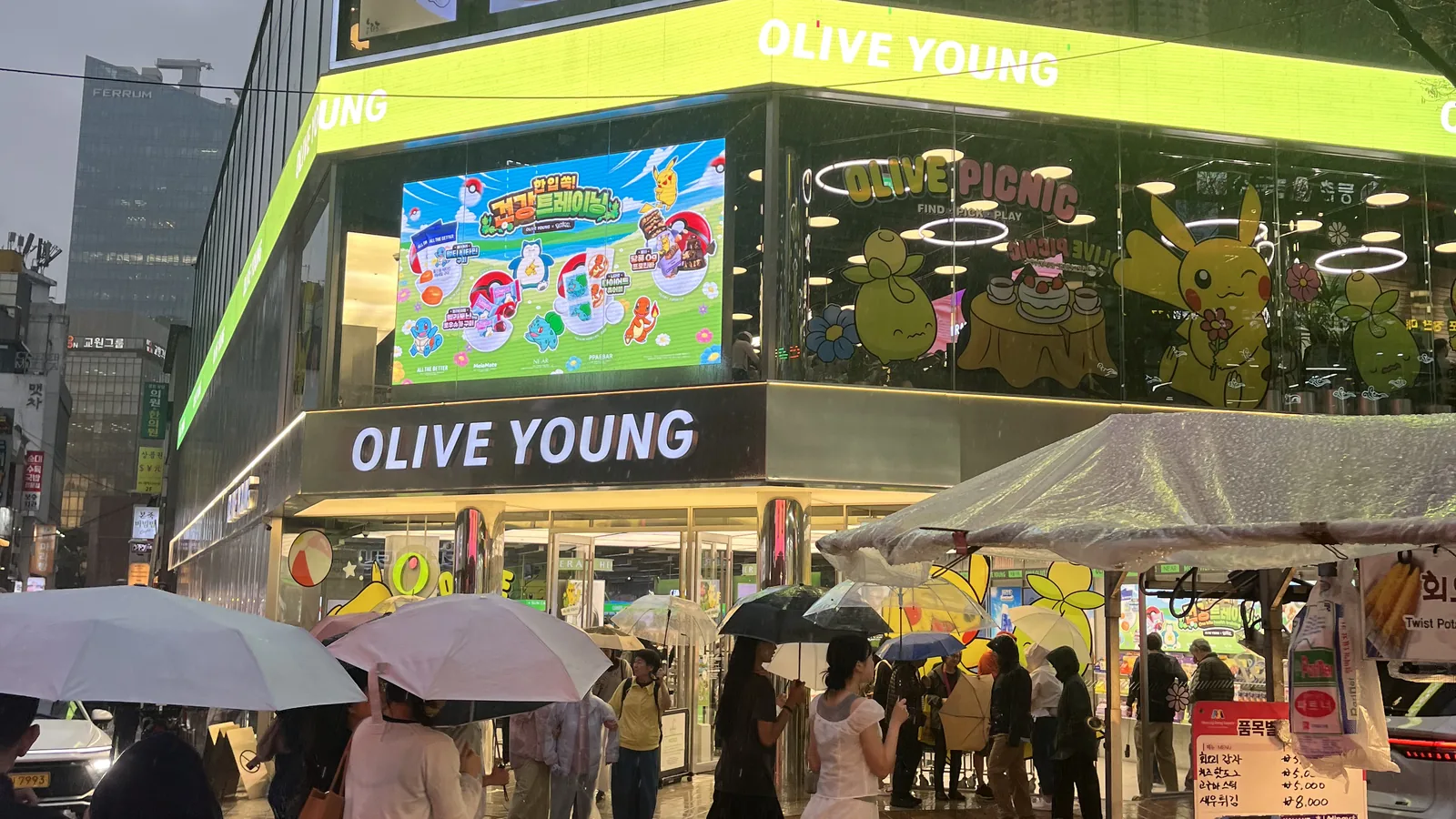 Olive Young Myeongdong corner store glowing on a rainy night street
