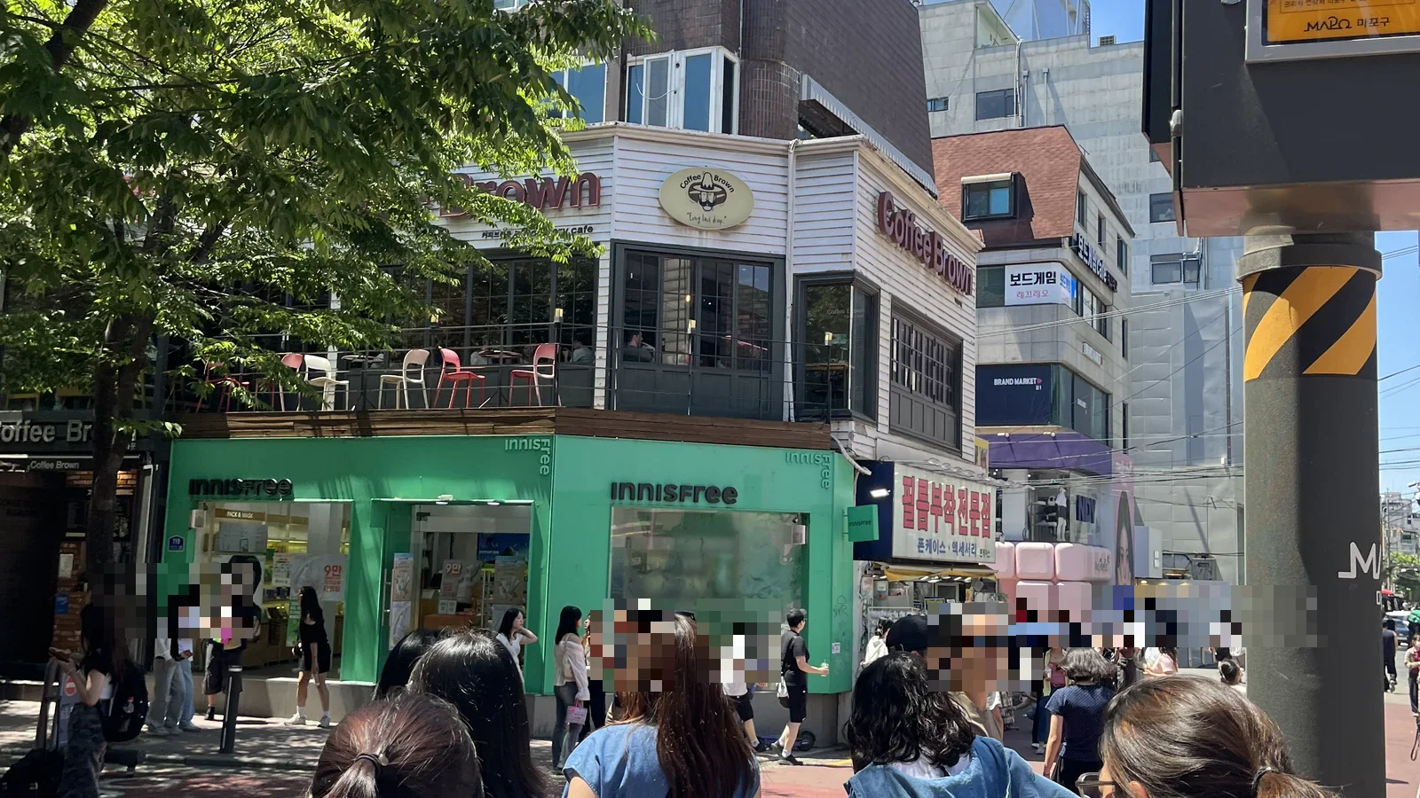 Innisfree storefront and a rooftop cafe on a busy Hongdae shopping street corner, Seoul