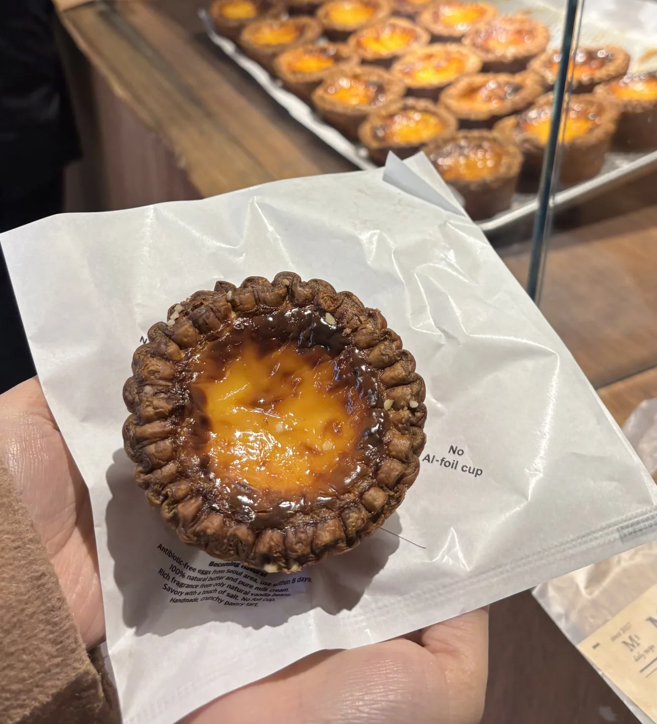 Seongsu-dong food guide Seoul: a salt egg tart with a burnt-sugar custard top held in paper at a Seongsu egg-tart shop