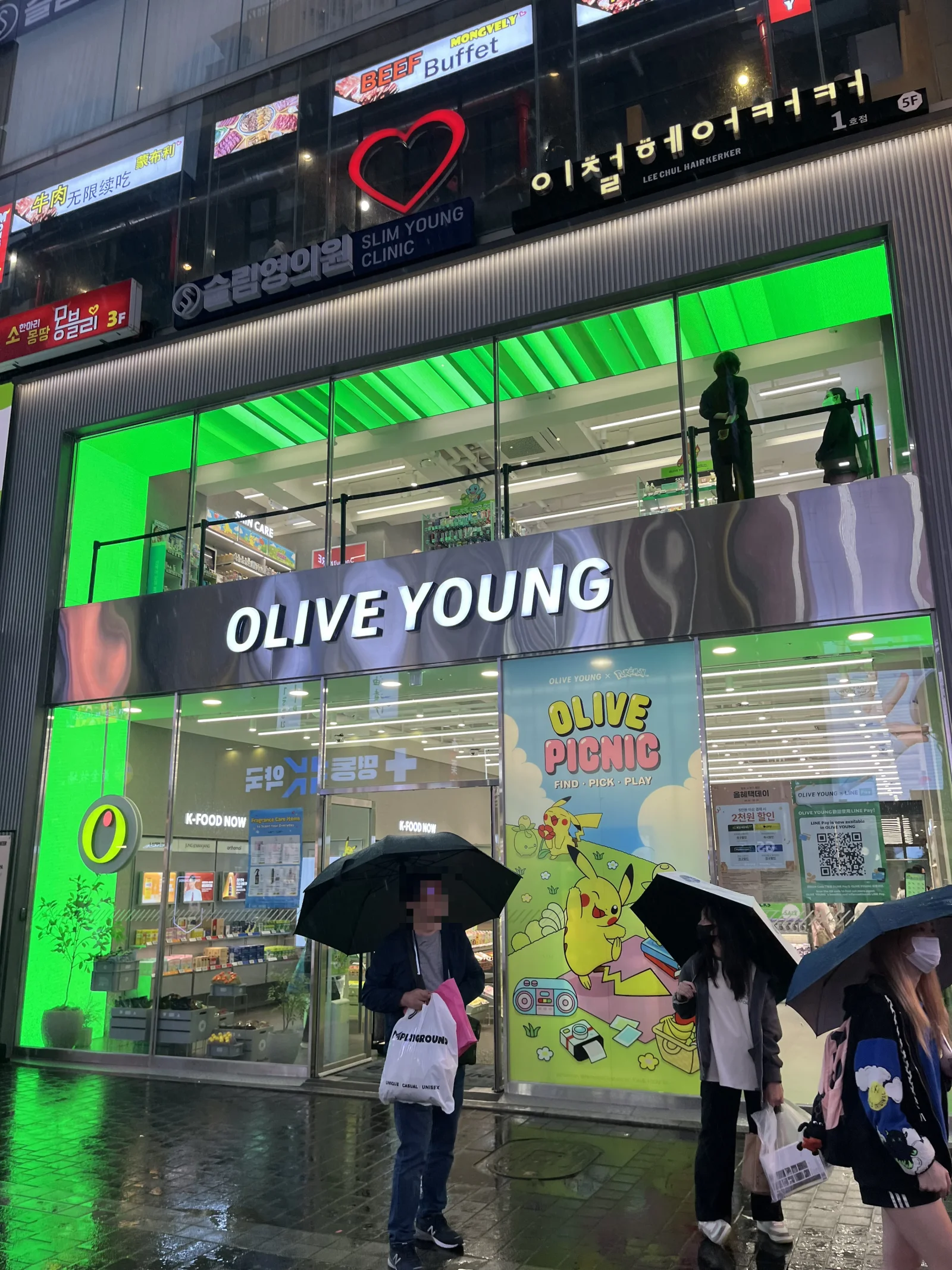 Olive Young Myeongdong branch at night with two glowing green floors and Pokemon collab window